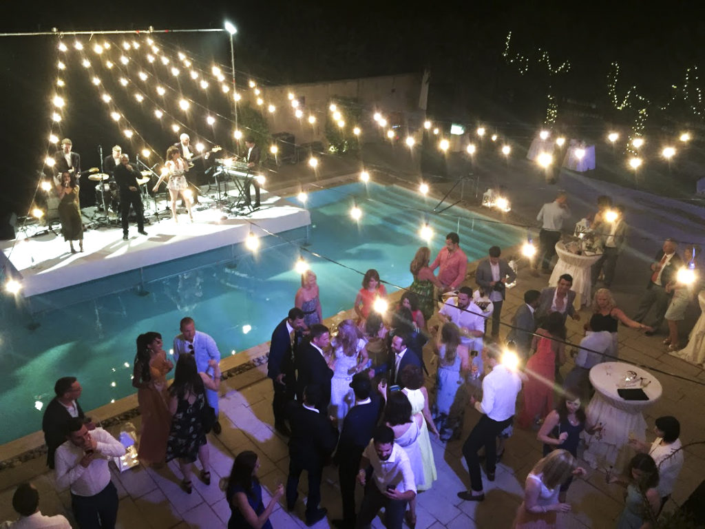 A band on a swimming pool with people dancing in front.