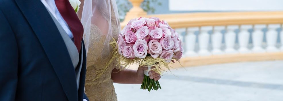 A bride with golden dress, walking into the Church with a pink rounded bridal bouquet.