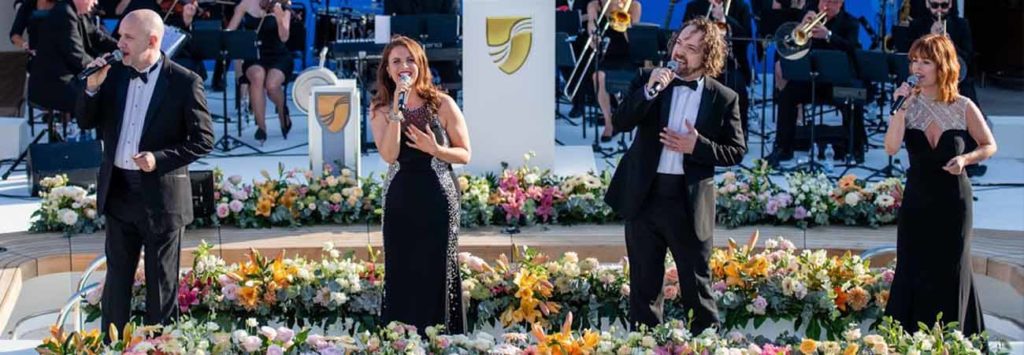 Four singers singing on an artificial bridge with flowers surrounding them