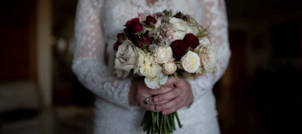 A bride holding a bridal bouquet with burgundy roses.