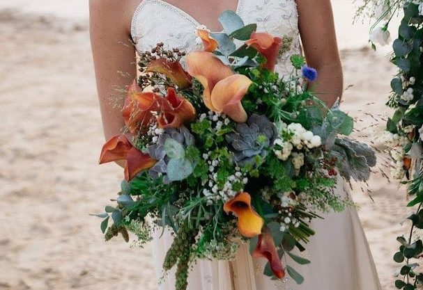 A boho styled bridal bouquet with a lot of foliage and orange hued flowers.