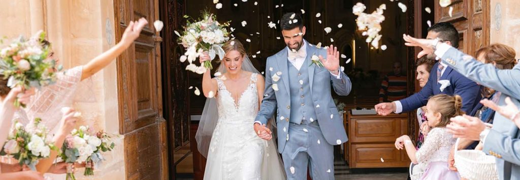 A newly married couple coming out from the Church with petals being thrown.