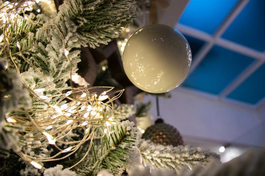 A cluster of lights on a snowy Christmas tree shining through a white bauble.