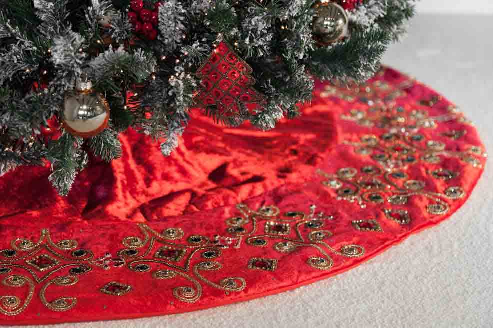 A red handcrafted Christmas tree skirt under a snowy artificial Christmas tree.